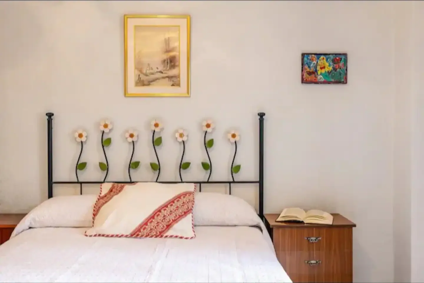 Dormitorio con cama de matrimonio y cabecero de forja con flores