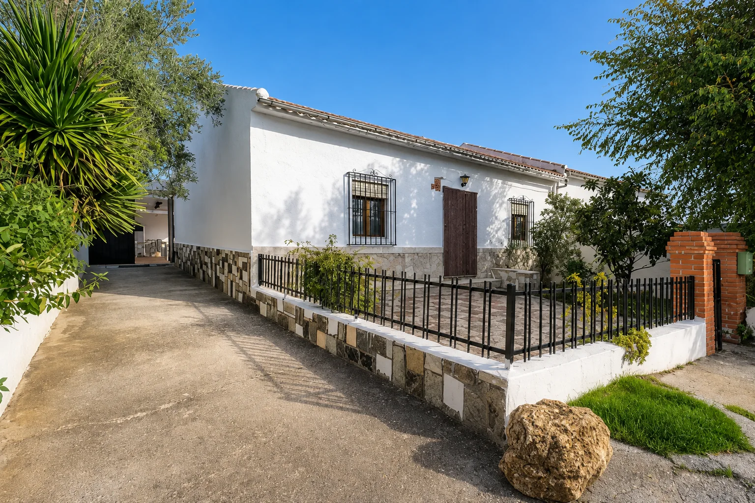 Fachada encalada de la casa, con zócalo de piedra, rejas y el jardín delantero